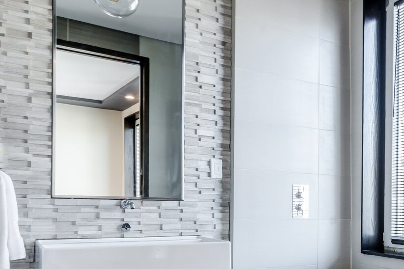 White bathroom with rectangular mirror against a stone wall.