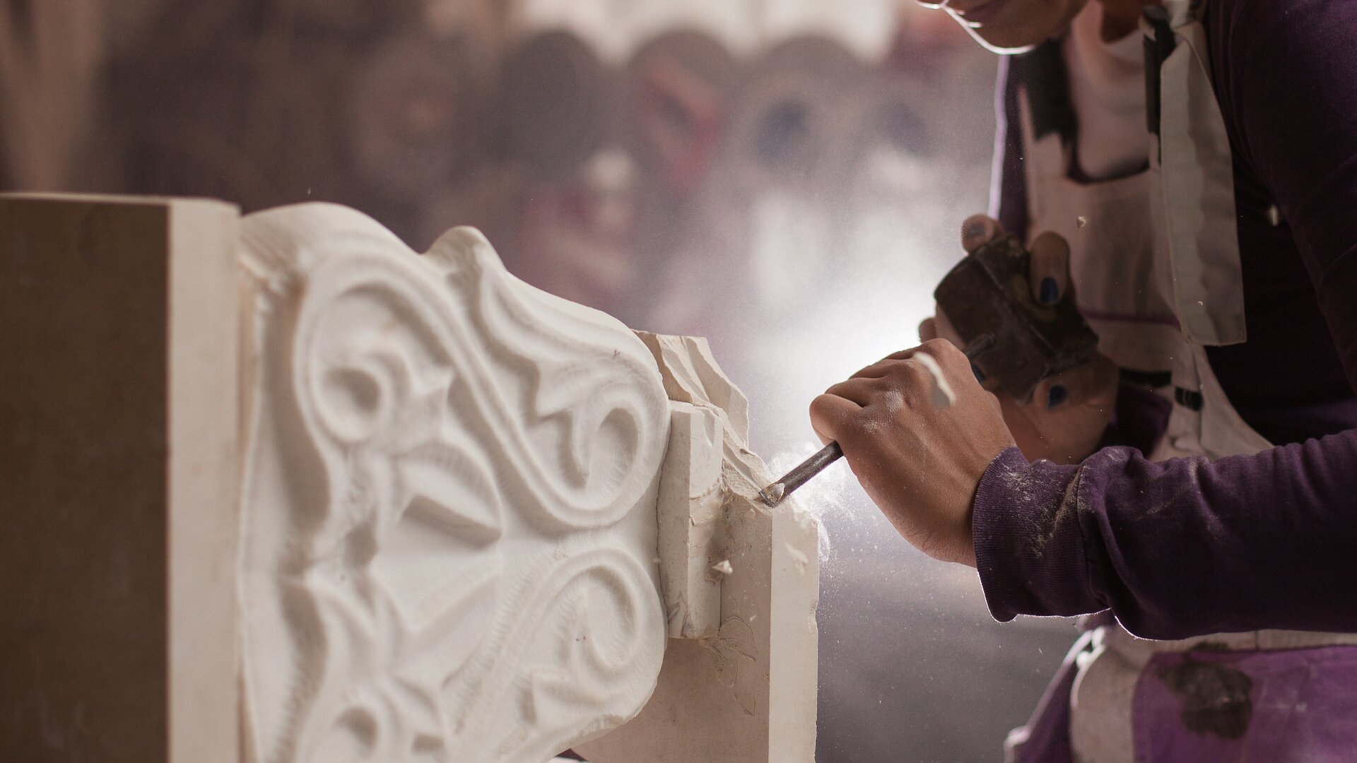 Close-up van een natuurstenen monument dat wordt bewerkt door een persoon met een beitel.