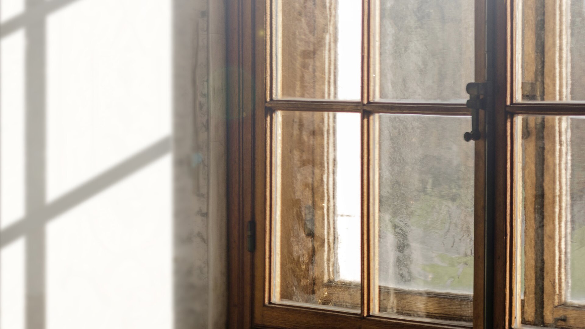 Vista su una doppia finestra in legno colpita dalla luce con la parete interna in ombra.
