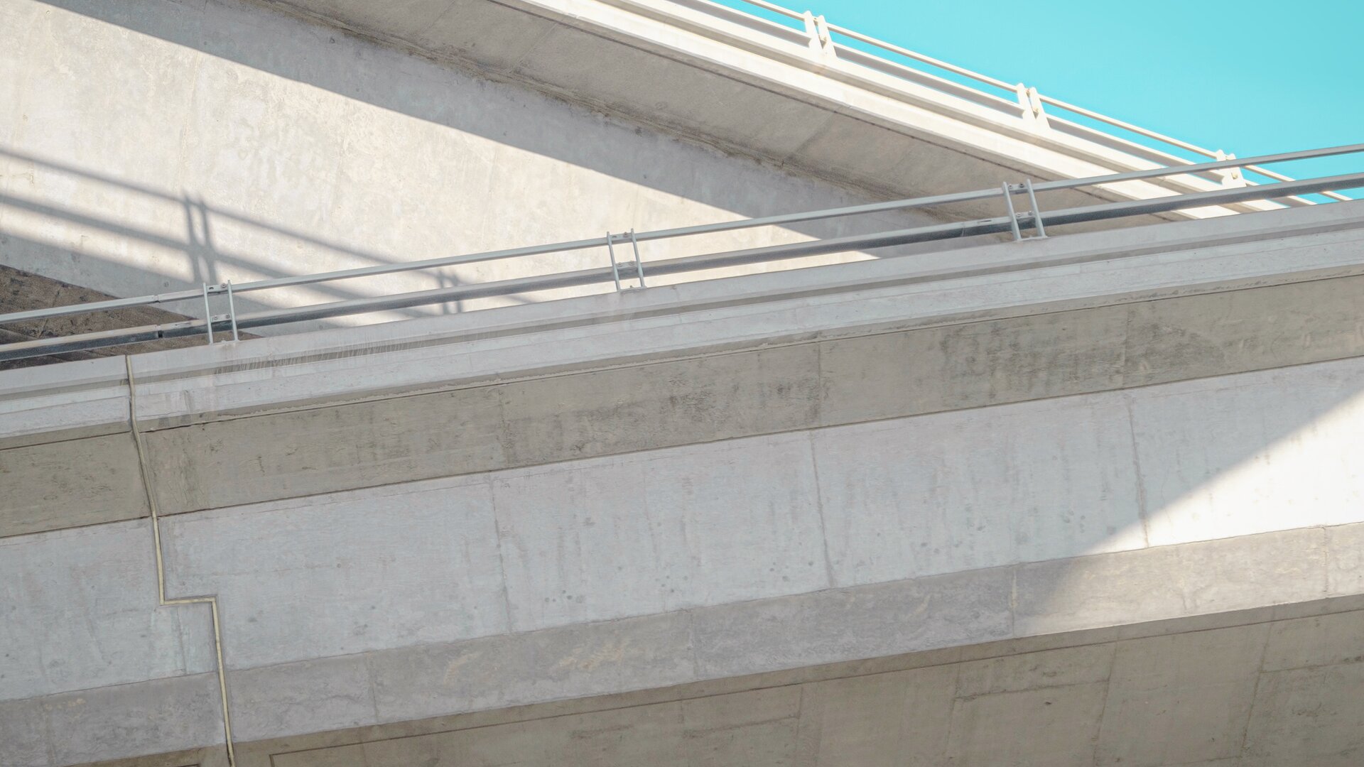 Close-up van twee elkaar kruisende betonnen relingen van een snelwegbrug met zichtbare bewegingsvoegen.