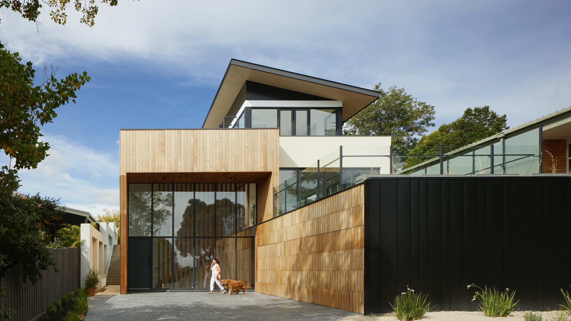Außenansicht eines modernen Hauses mit Baukörperanschlüssen in schwarzer und heller Holzoptik, sowie Glaselementen.