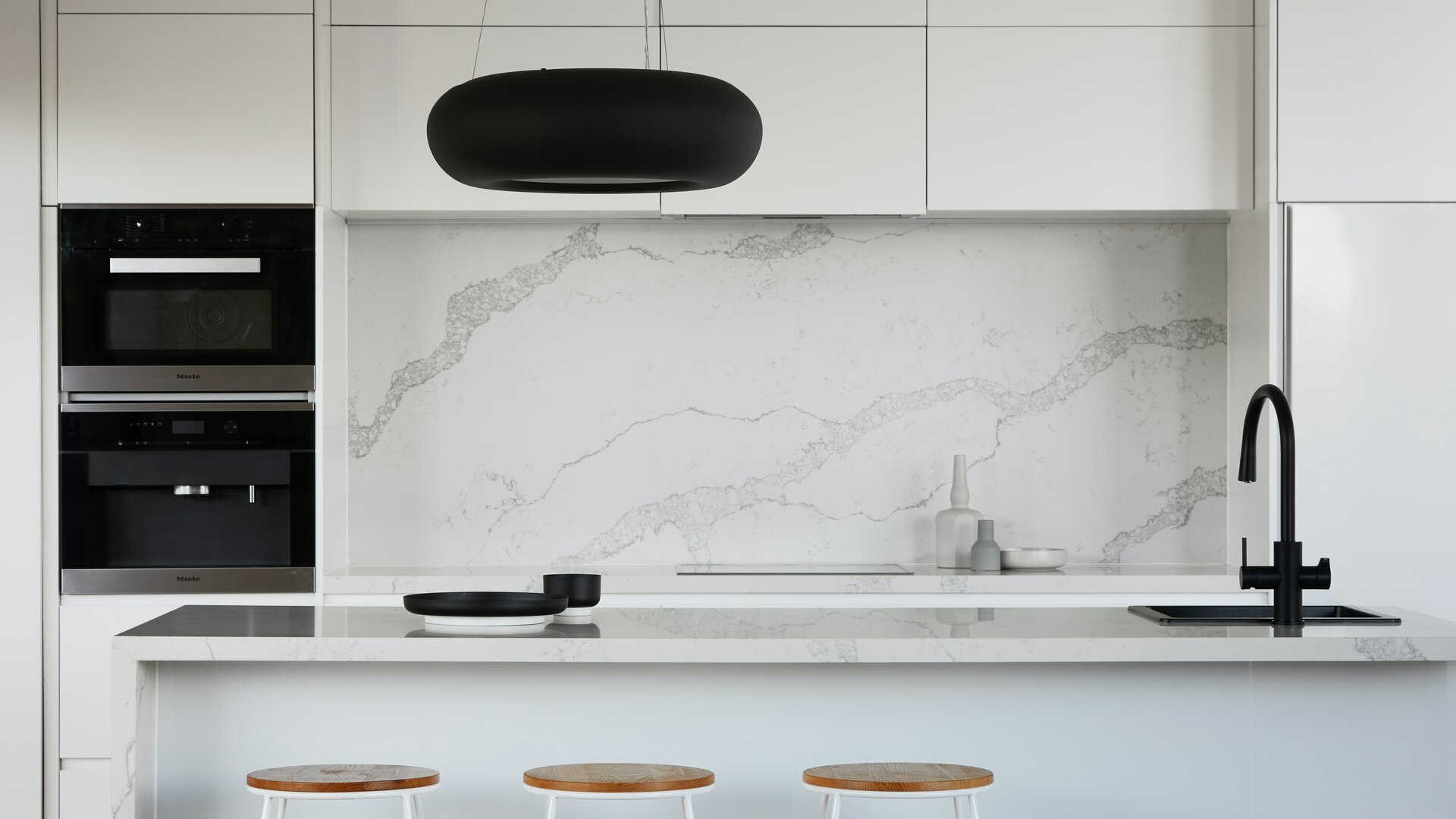Moderna cucina bianca con elementi neri e piano di lavoro in pietra naturale.