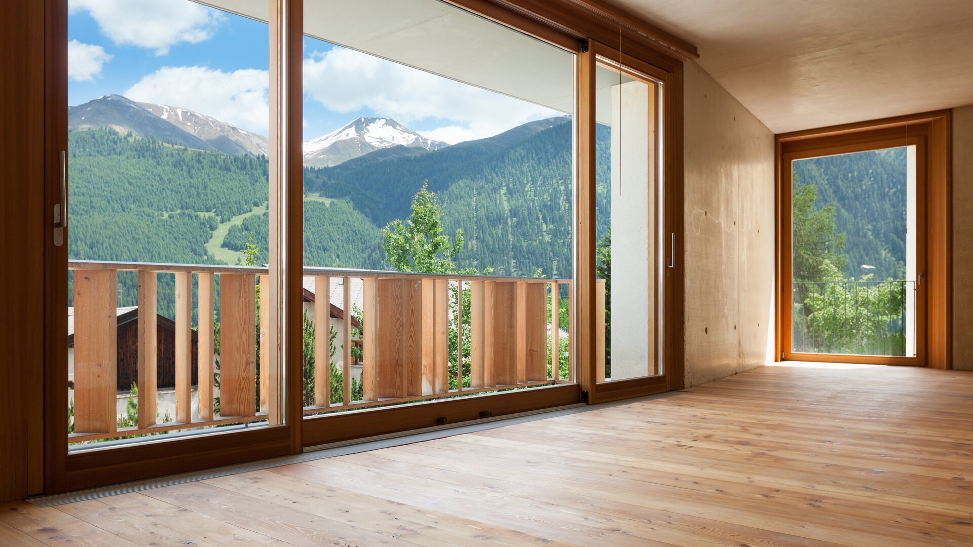 Moderner leerstehender Raum in heller Holzoptik mit großen Holzfenstern und Blick in die Natur.