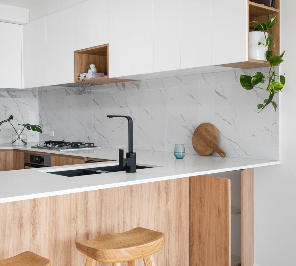 Bright kitchen with black elements, marble wall tiles and light wood facades