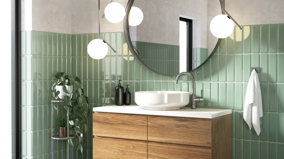 Modern bathroom with green tiles, large round mirror and bathroom cabinet with wooden front.