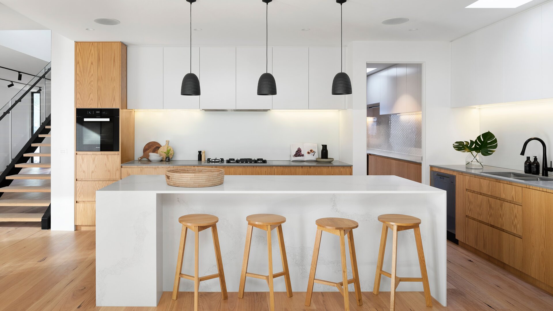 Moderne weiße Küche mit Holzelementen, weißer Kücheninsel und Holzhocker.